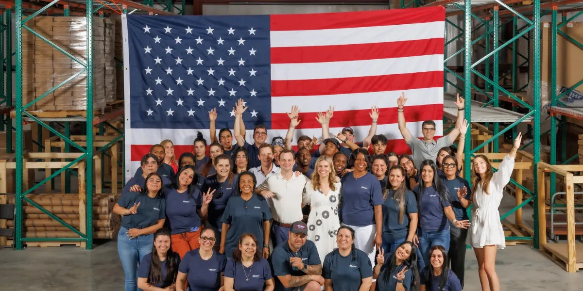 Employees of an American flag store gathered in front of a massive U.S. flag inside their warehouse