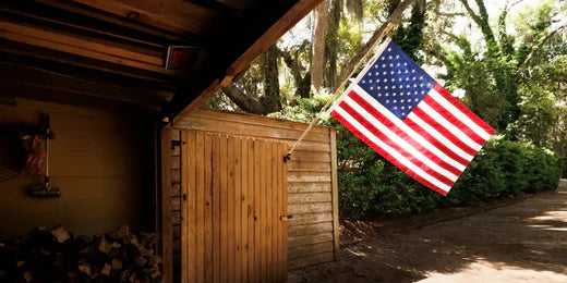 Durable American flag waving outside a rustic wooden shed in a sunlit forest setting